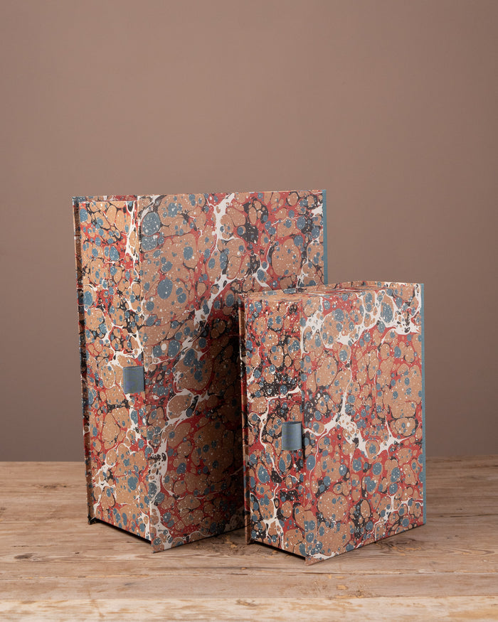 Two decorative boxes with marbled design on a wooden surface and brown background