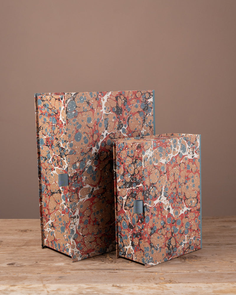 Two decorative boxes with marbled design on a wooden surface and brown background