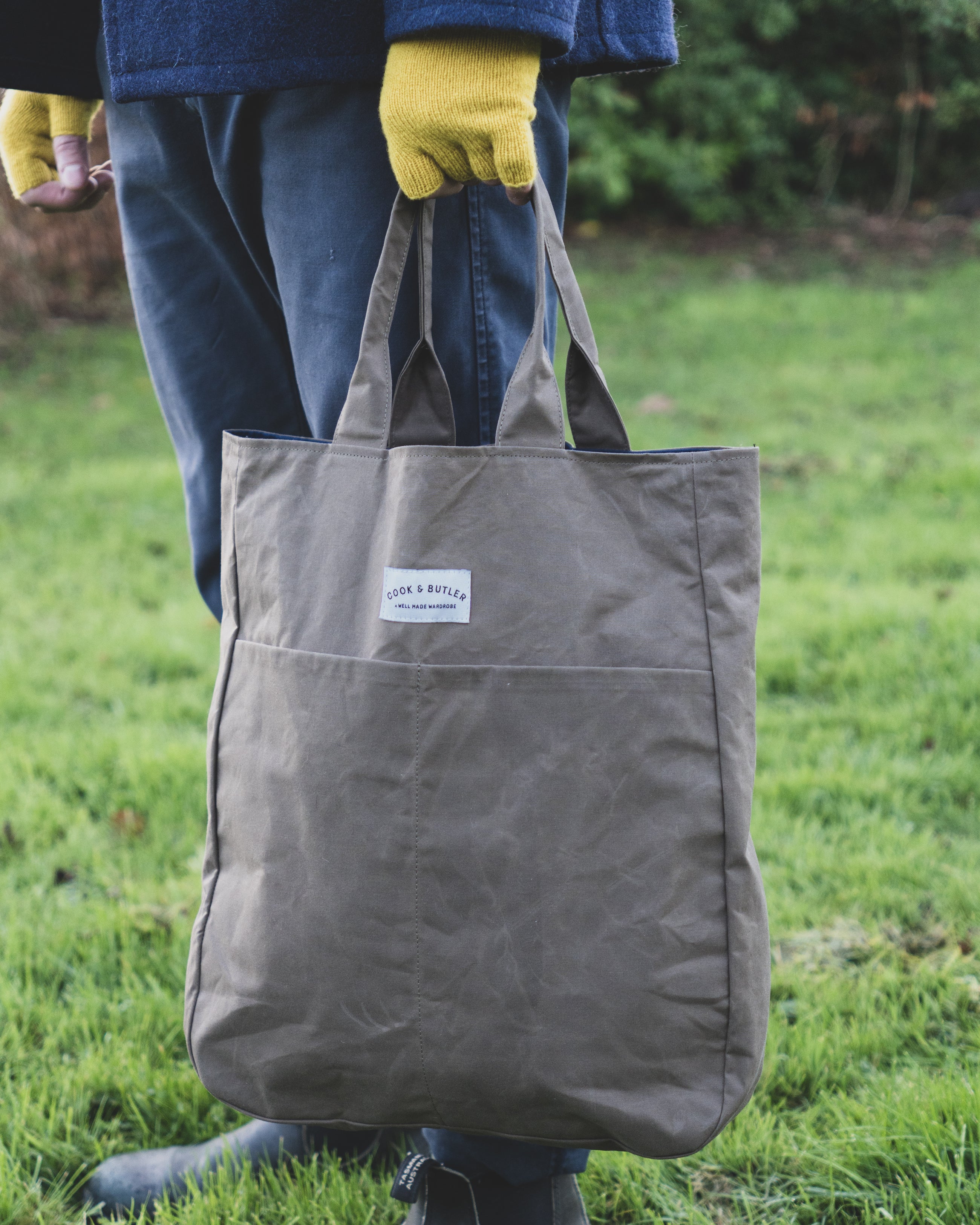 Person with yellow gloves holding a 'Cook and Butler' tote bag.
