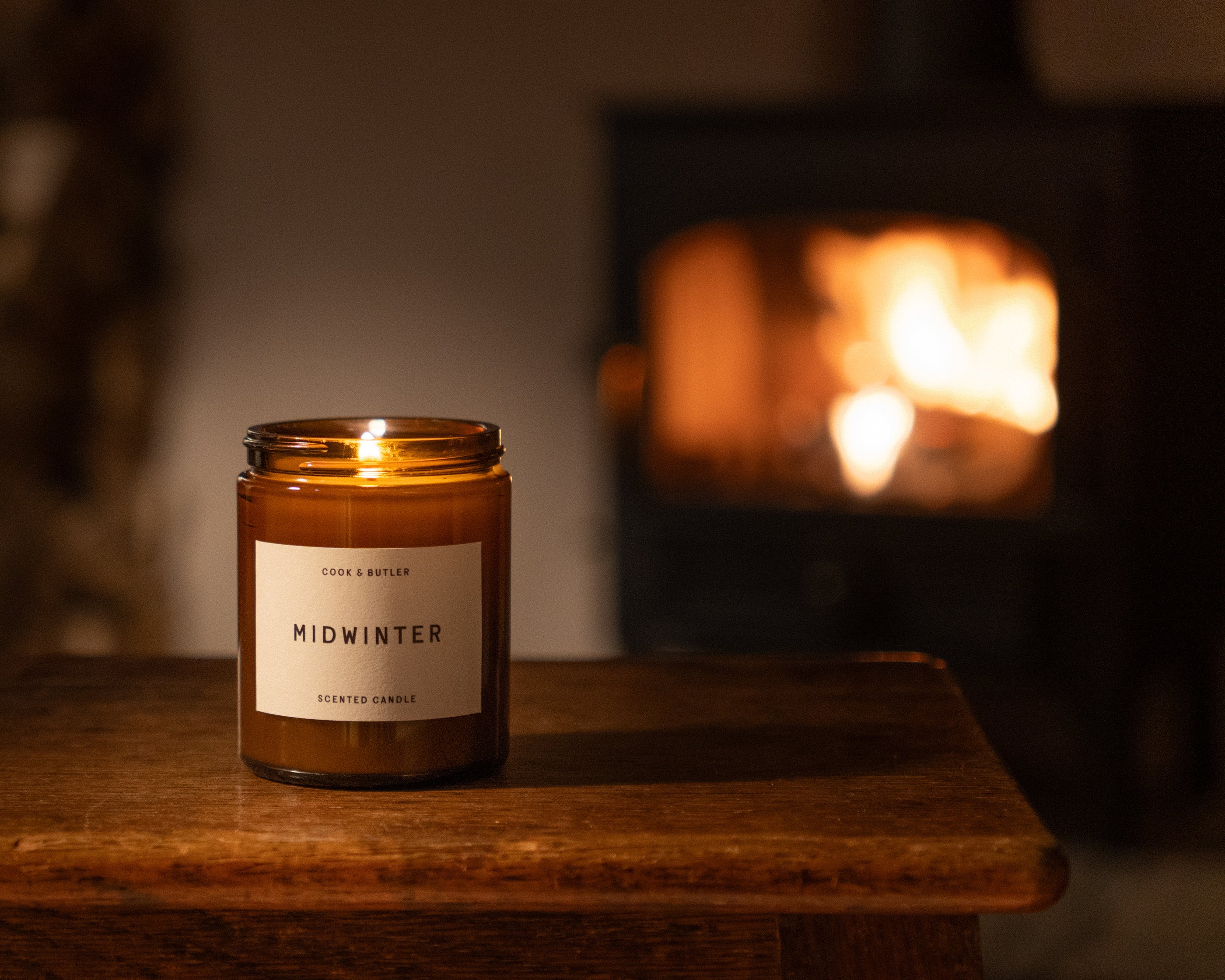 Chistmas candle labelled 'Midwinter' on a wooden surface with a fireplace in the background