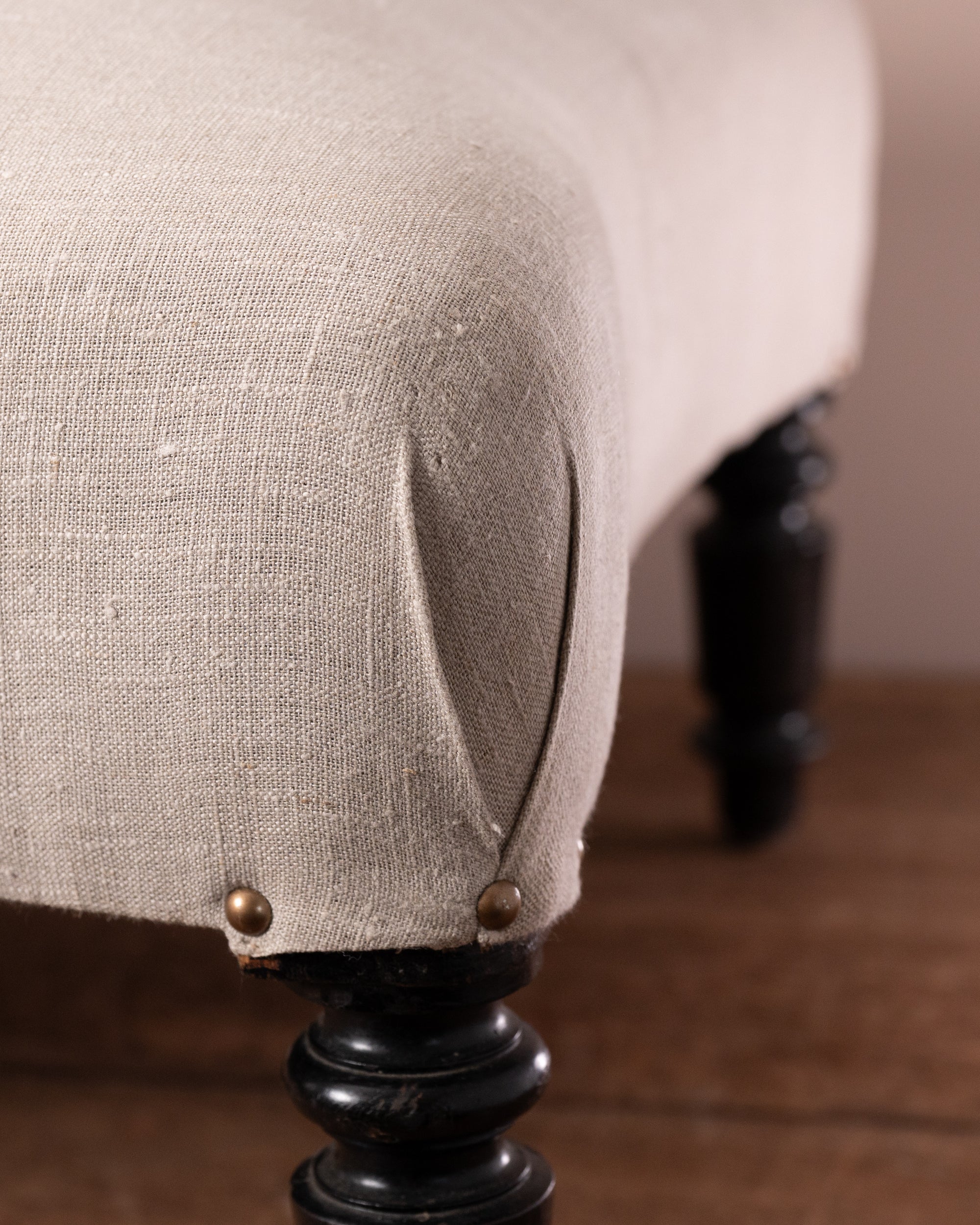 Close-up of a beige upholstered chair with dark wooden legs on a wooden floor.