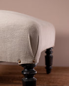 Close-up of a beige upholstered chair with dark wooden legs against a beige wall.