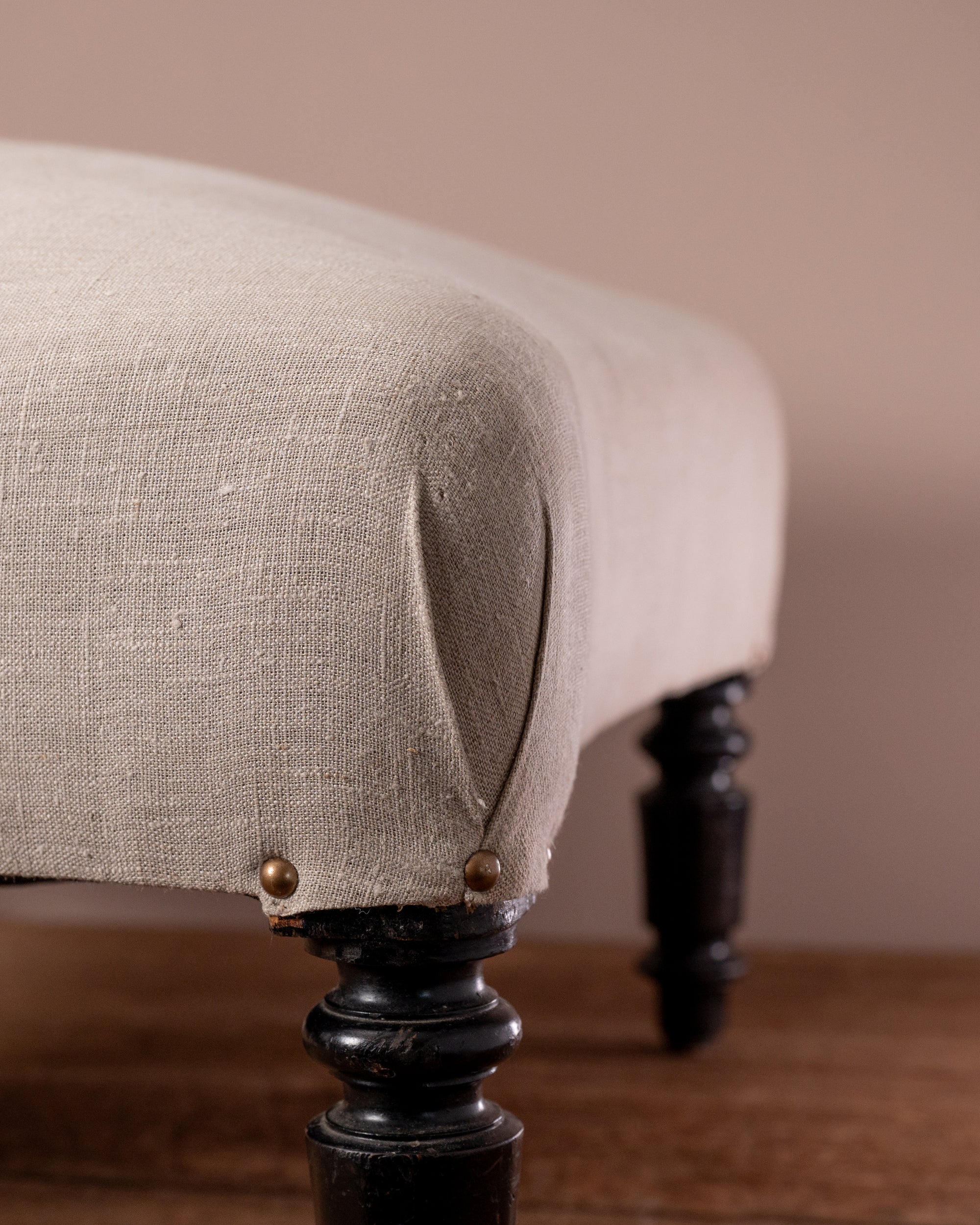 Close-up of a beige upholstered chair with dark wooden legs against a beige wall.