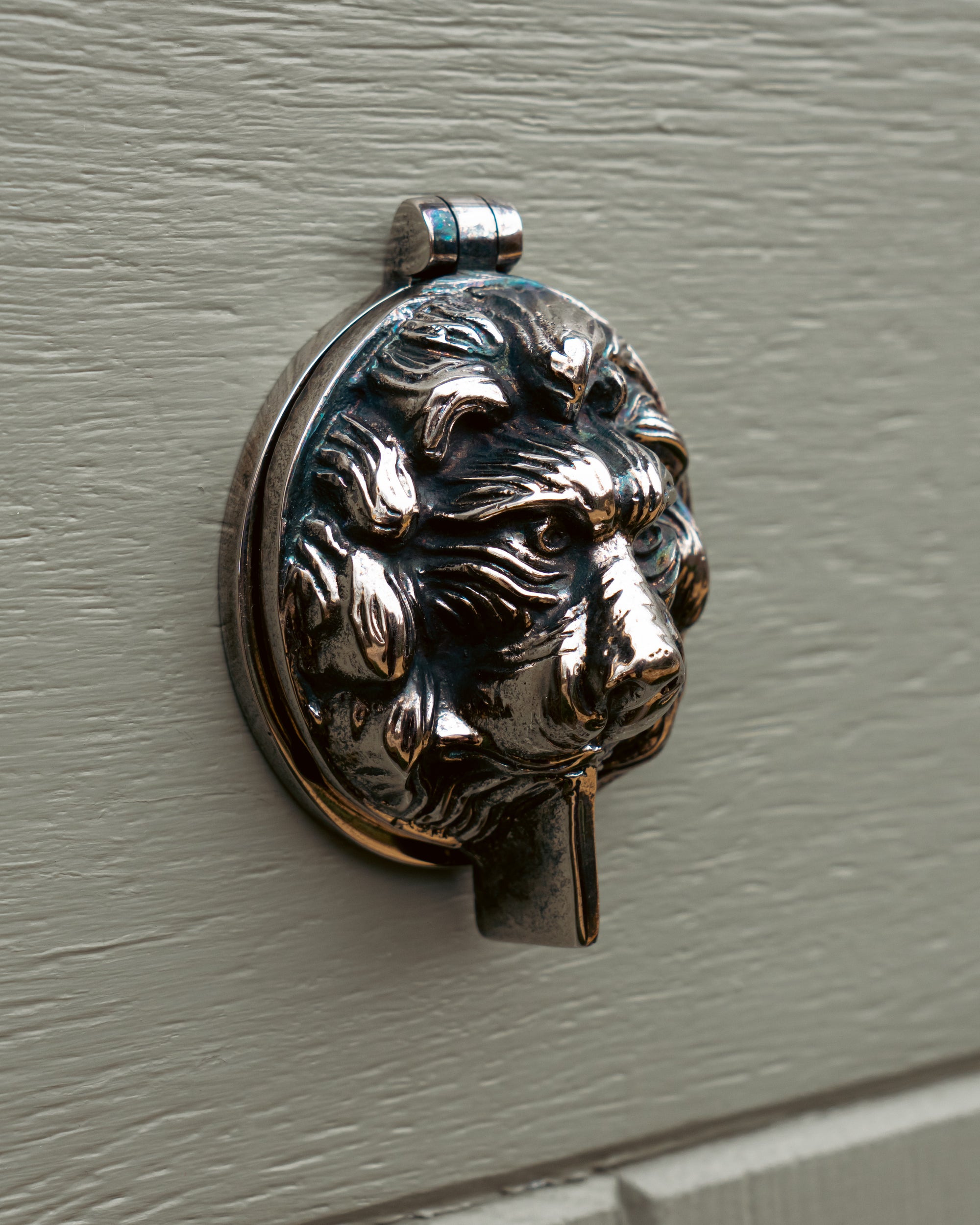 Decorative keyhole cover shaped like a lion's head on a grey door.