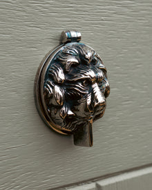 Decorative keyhole cover shaped like a lion's head on a grey door.