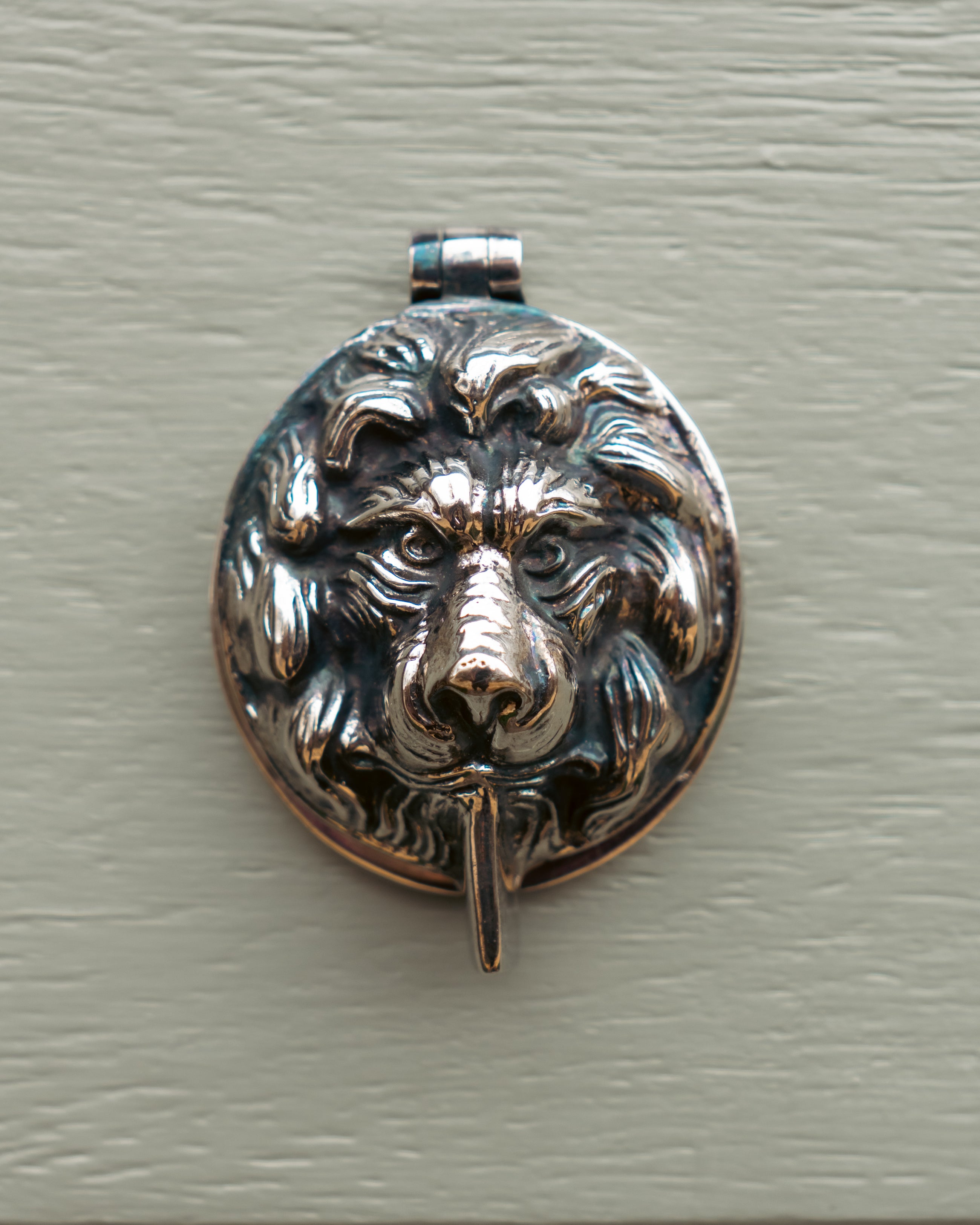 Silver lion head pendant on a textured grey background