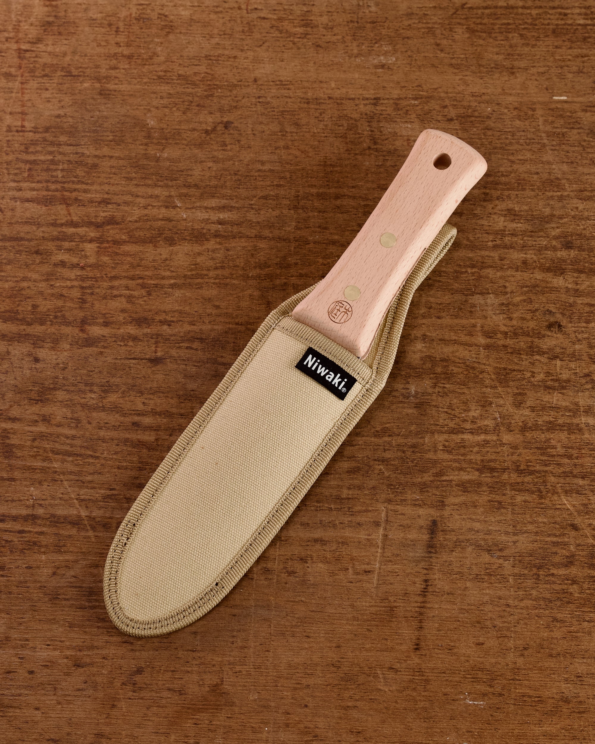 Niwaki Hori Hori garden knife in a canvas sheath on a wooden background