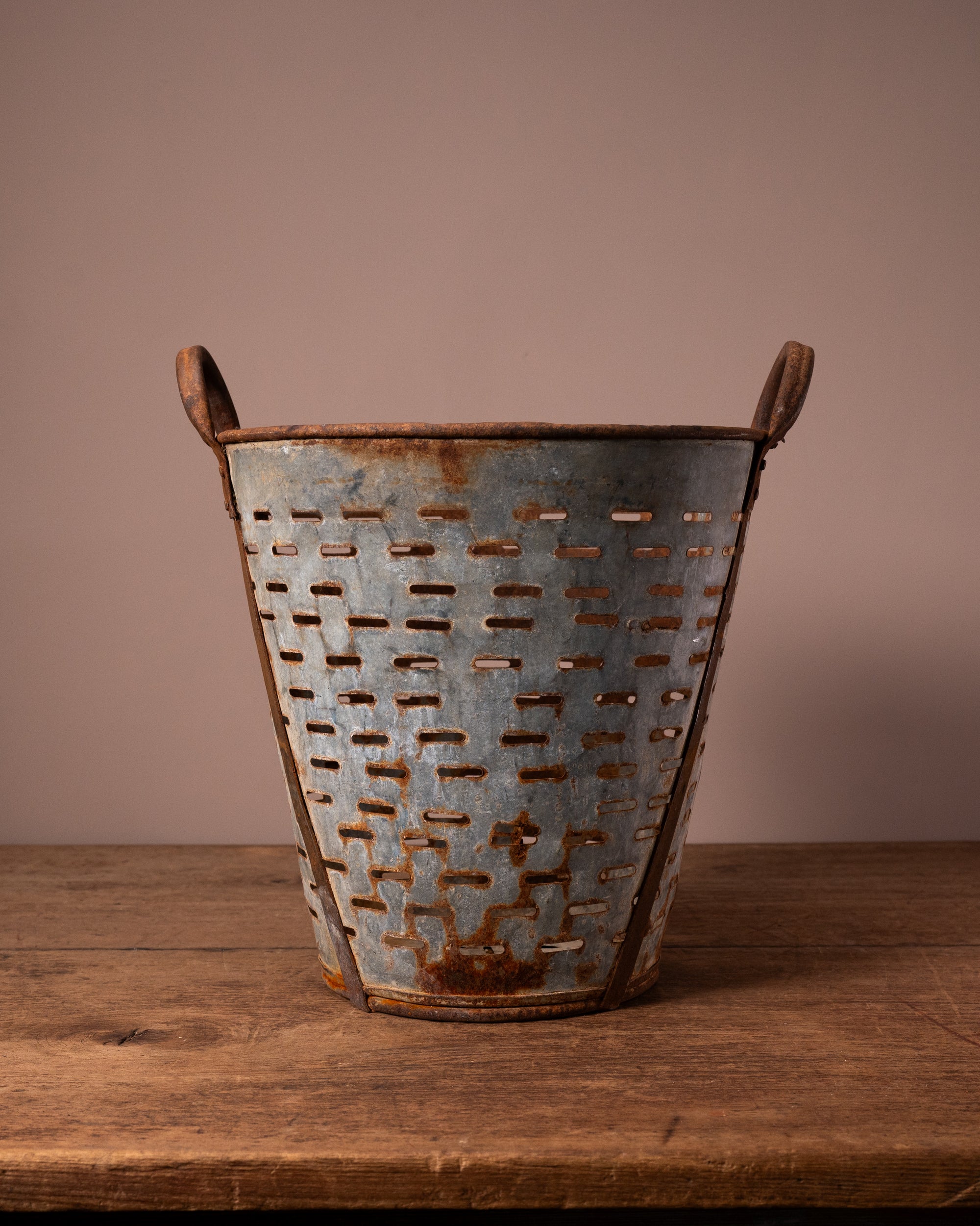 Rustic metal basket with handles on a wooden surface against a brown background