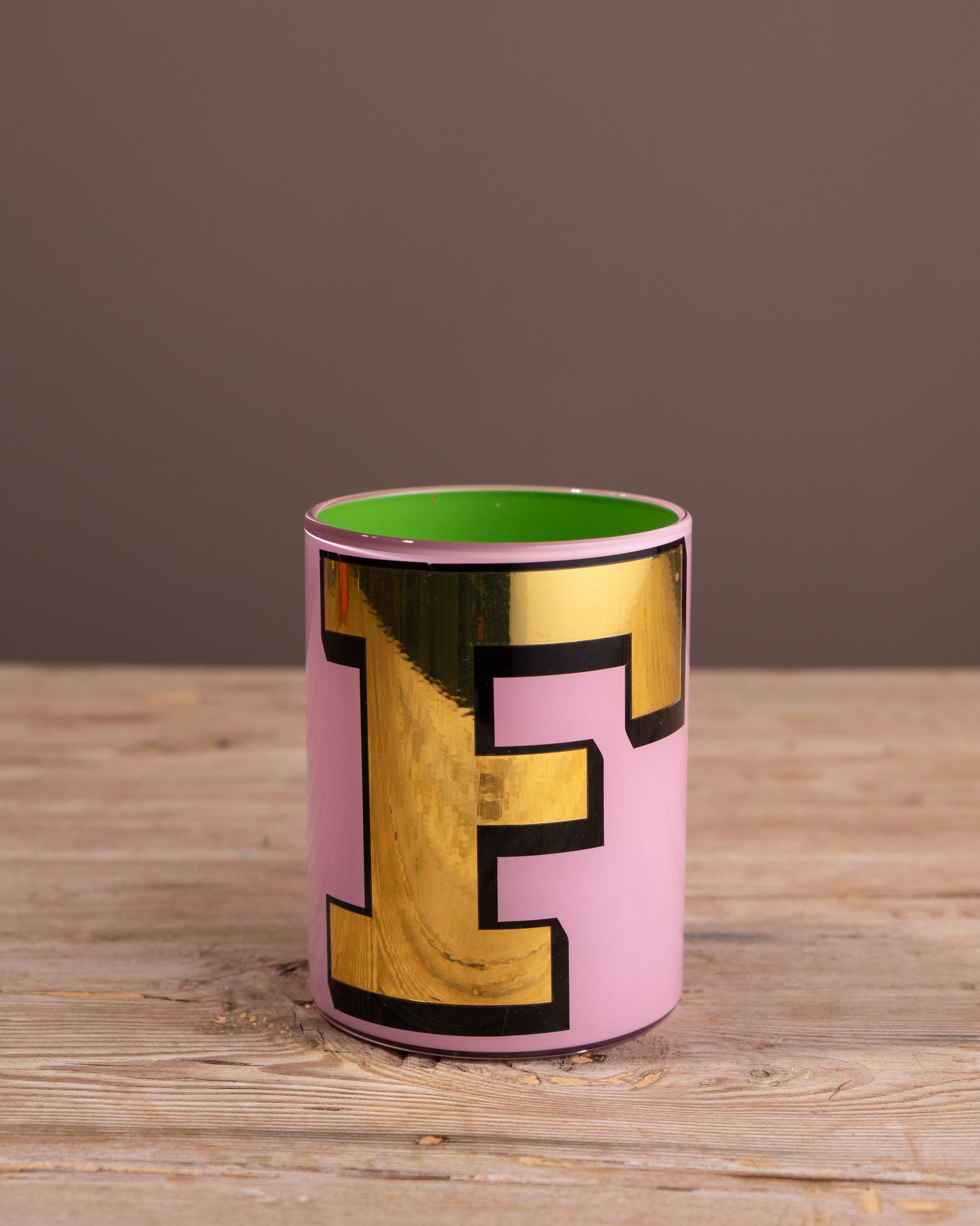 Pink cup with gold letter 'F' on a wooden surface