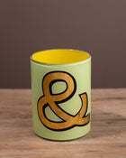 Green glass beaker with a brown ampersand design on a wooden surface