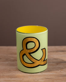 Green glass beaker with a brown ampersand design on a wooden surface