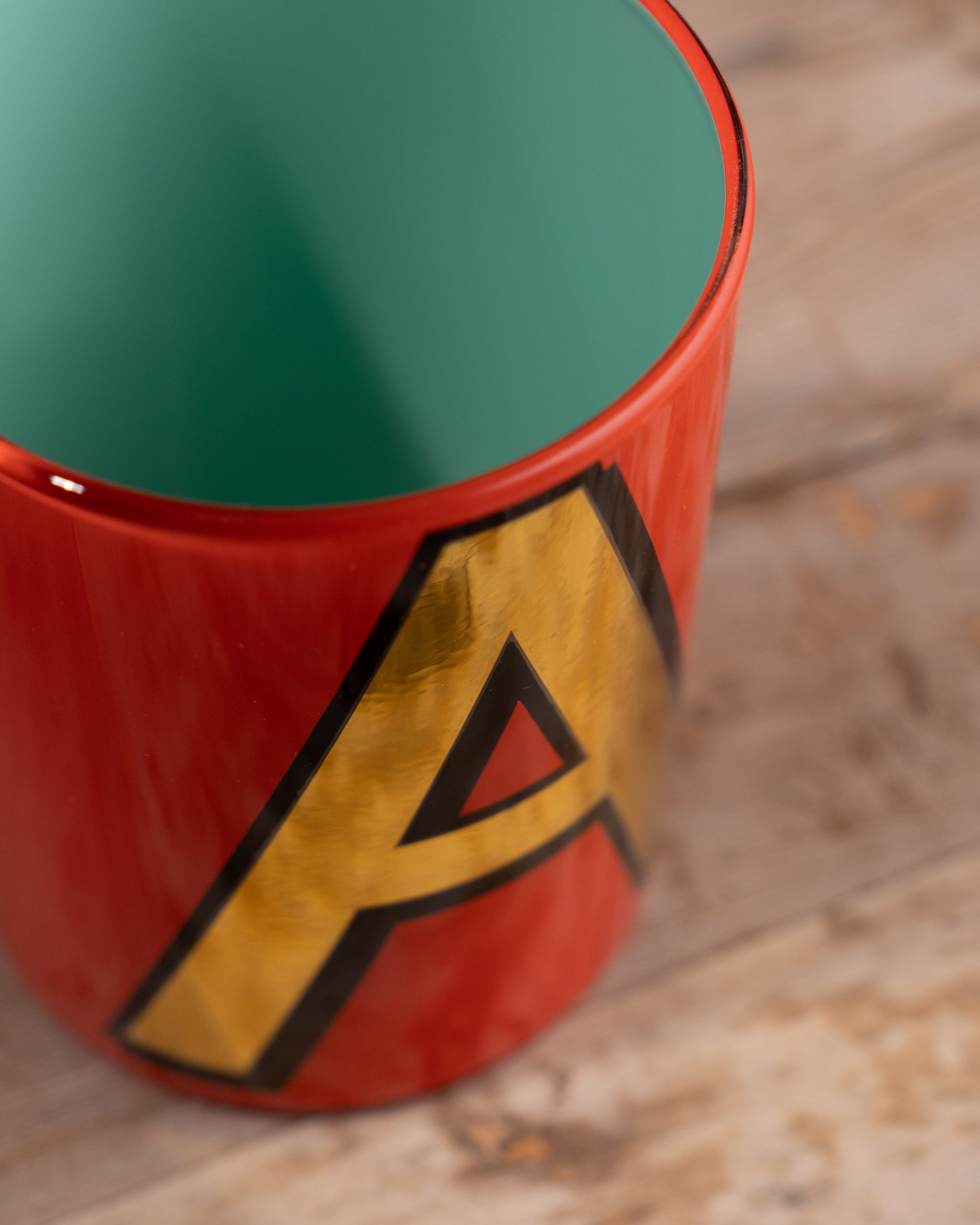 Close-up of a red Bridie Hall pot with a yellow 'A' logo on a wooden surface