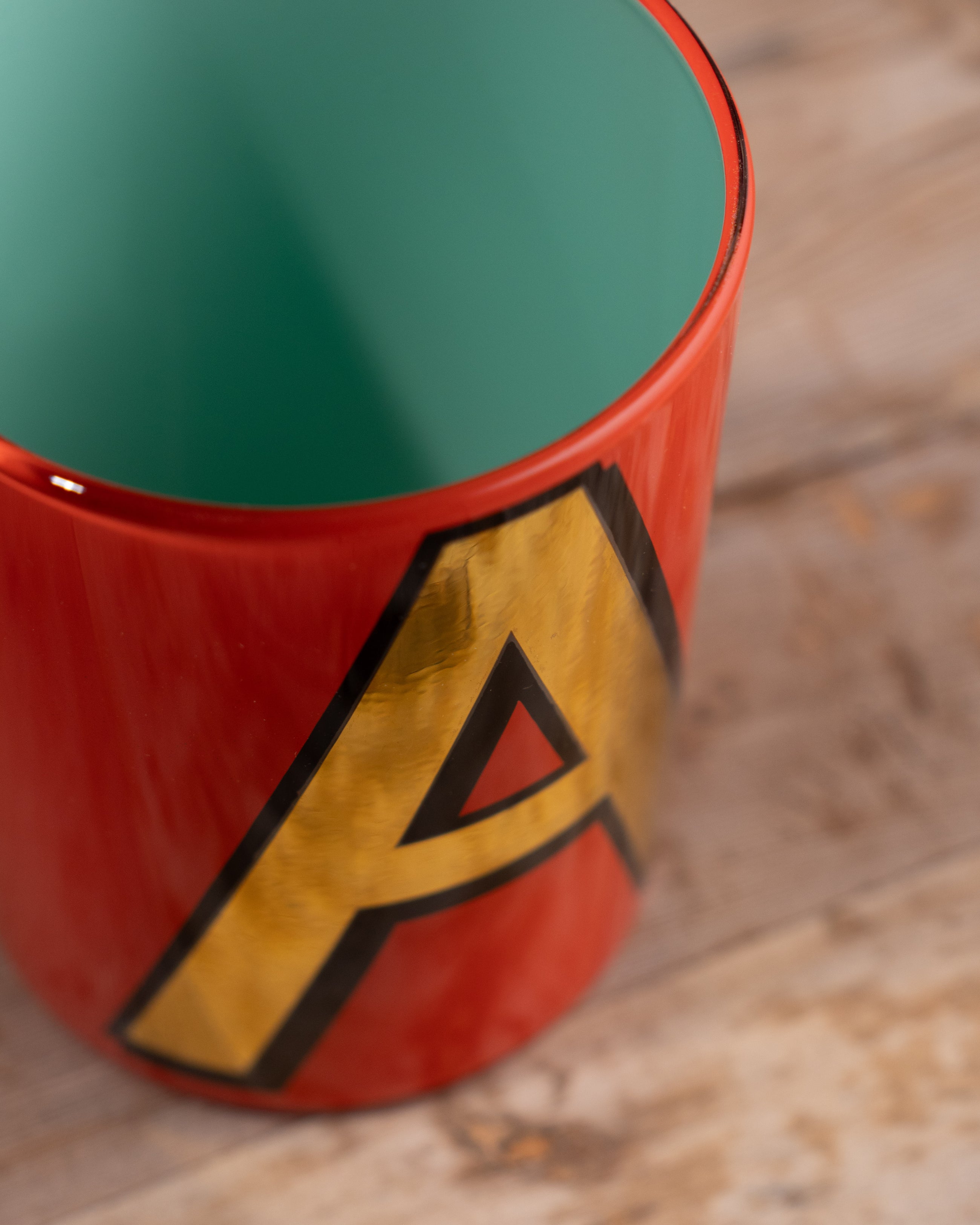 Close-up of a red Bridie Hall pot with a yellow 'A' logo on a wooden surface