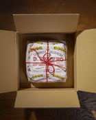 Panettone wrapped in paper with red string in an open cardboard box.