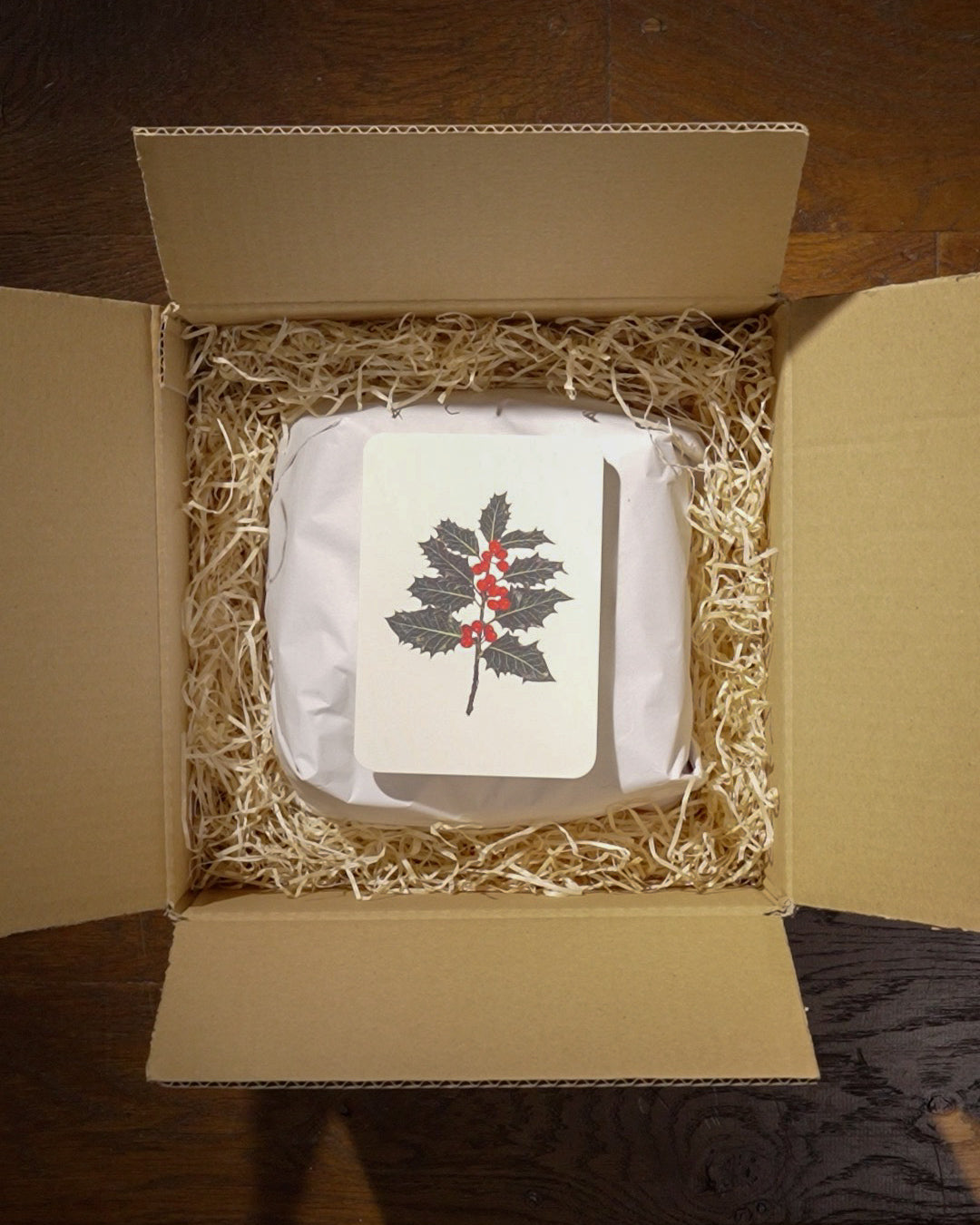 Product inside a cardboard box with decorative card on a wooden surface