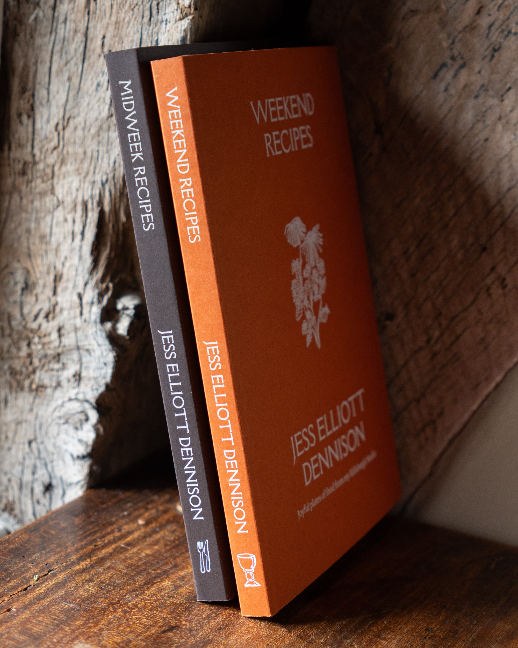 Two recipe books titled 'Weekend Recipes' and 'Midweek Recipes' by Jess Elliott Dennison on a wooden surface.