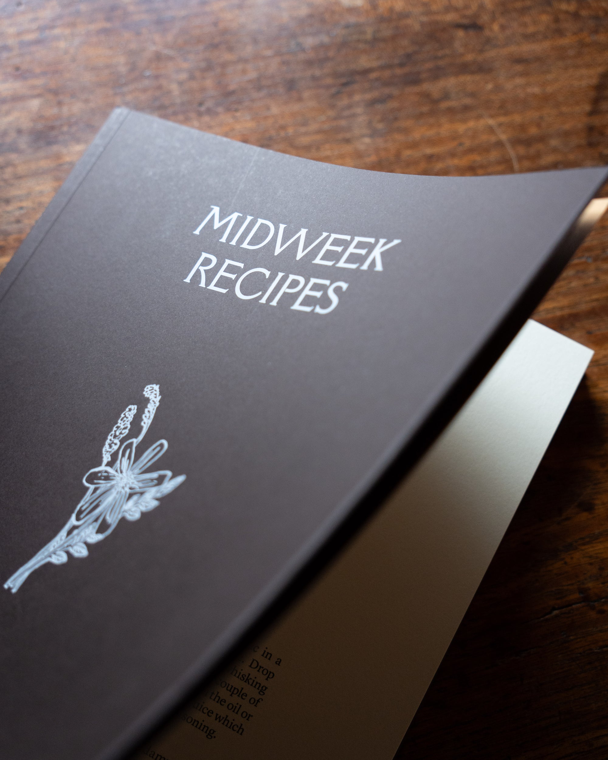 Cookbook titled 'Midweek Recipes' on a wooden surface