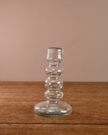 Clear glass candle holder on a wooden surface with a beige background