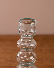 Clear glass candle holder on a wooden surface with a beige background