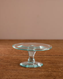 Clear glass cake stand on a wooden surface with a beige background