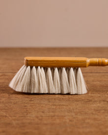 Wooden cleaning brush with white bristles on a wooden surface