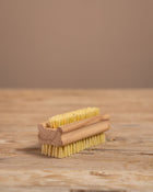 wooden nail brush with yellow bristles on a wooden surface and brown background