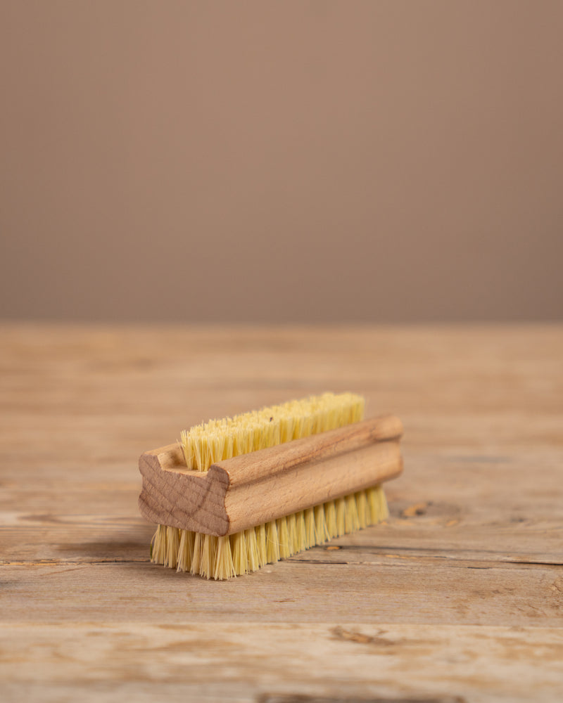 wooden nail brush with yellow bristles on a wooden surface and brown background