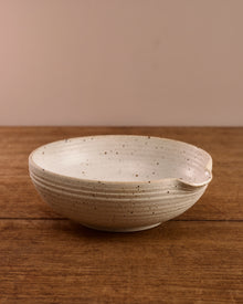 Speckled ceramic mixing bowl on a wooden surface with a beige background