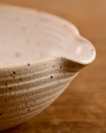 Speckled ceramic mixing bowl on a wooden surface with a beige background