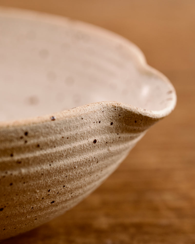 Speckled ceramic mixing bowl on a wooden surface with a beige background