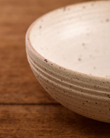 Speckled ceramic mixing bowl on a wooden surface with a beige background