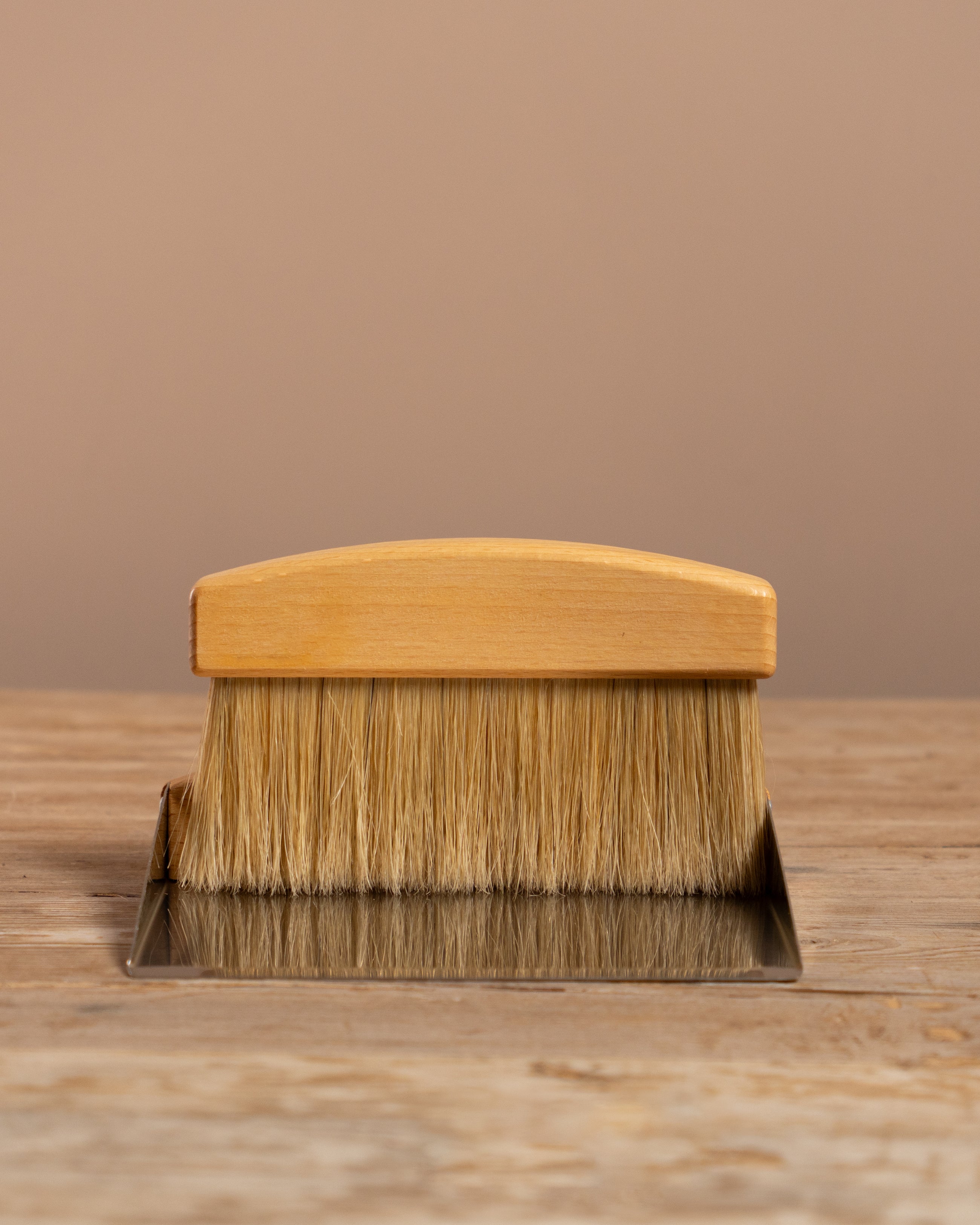 Wooden brush with metal dustpan on a wooden surface