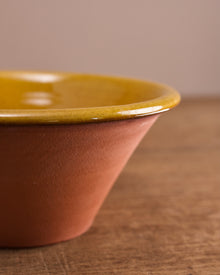 Terracotta bowl with yellow glazed interior  on a wooden surface.