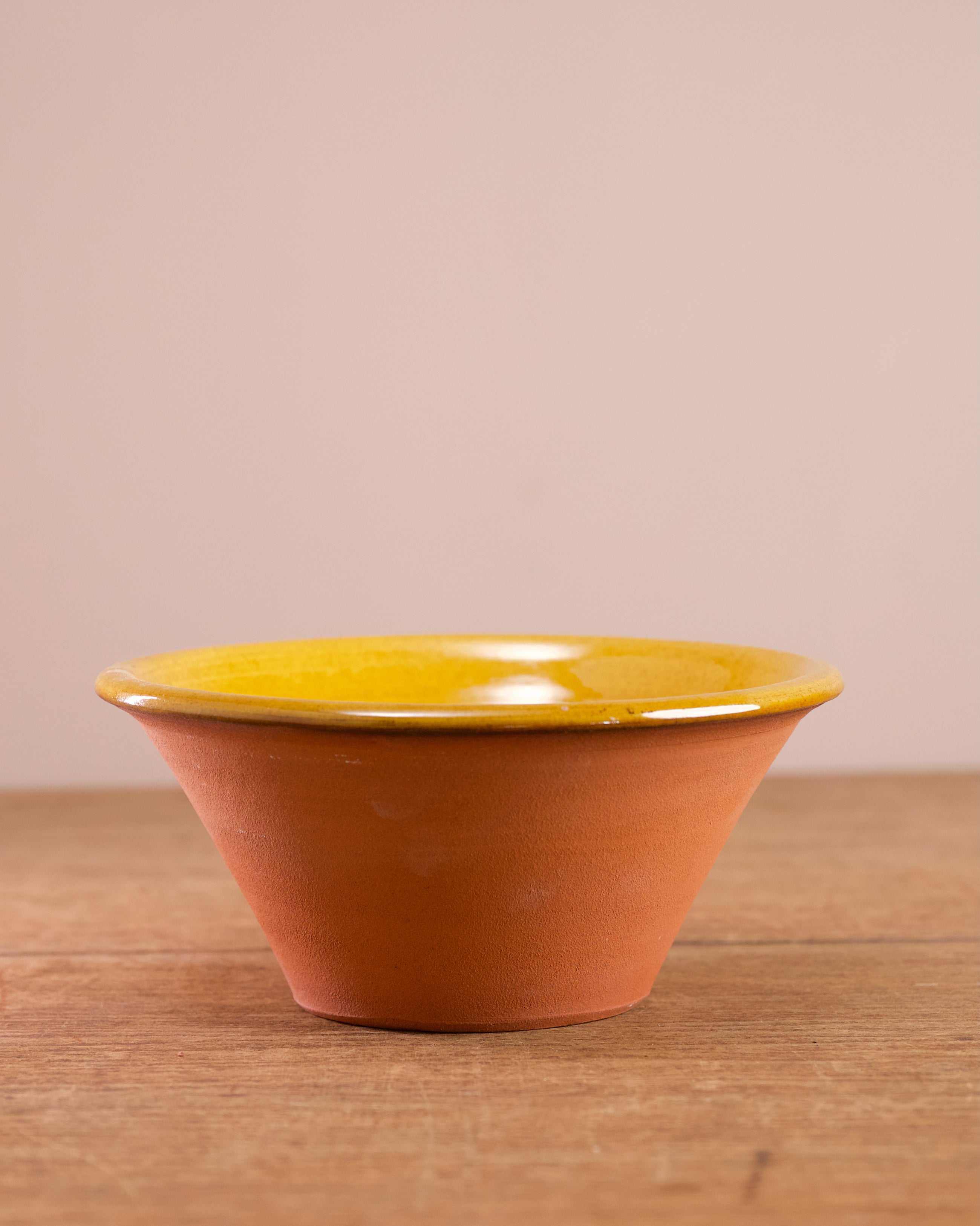 Ceramic bowl with yellow glazed interior and terracotta exterior on a wooden surface.