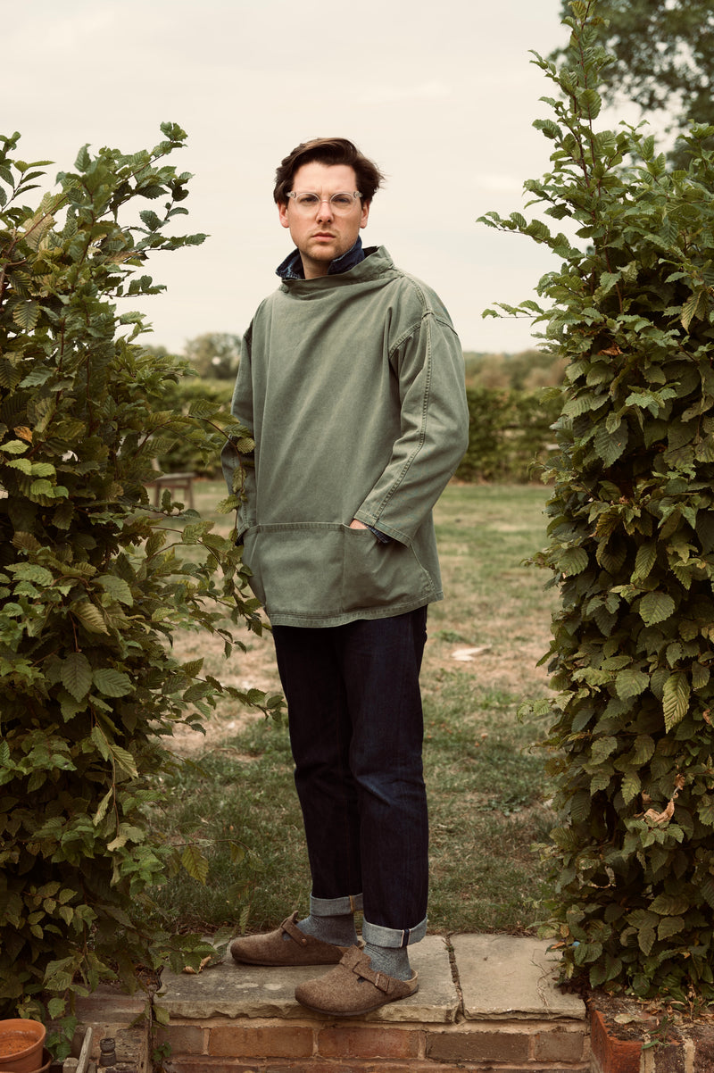 Person wearing a green Cook & Butler smock standing between two rows of plants.