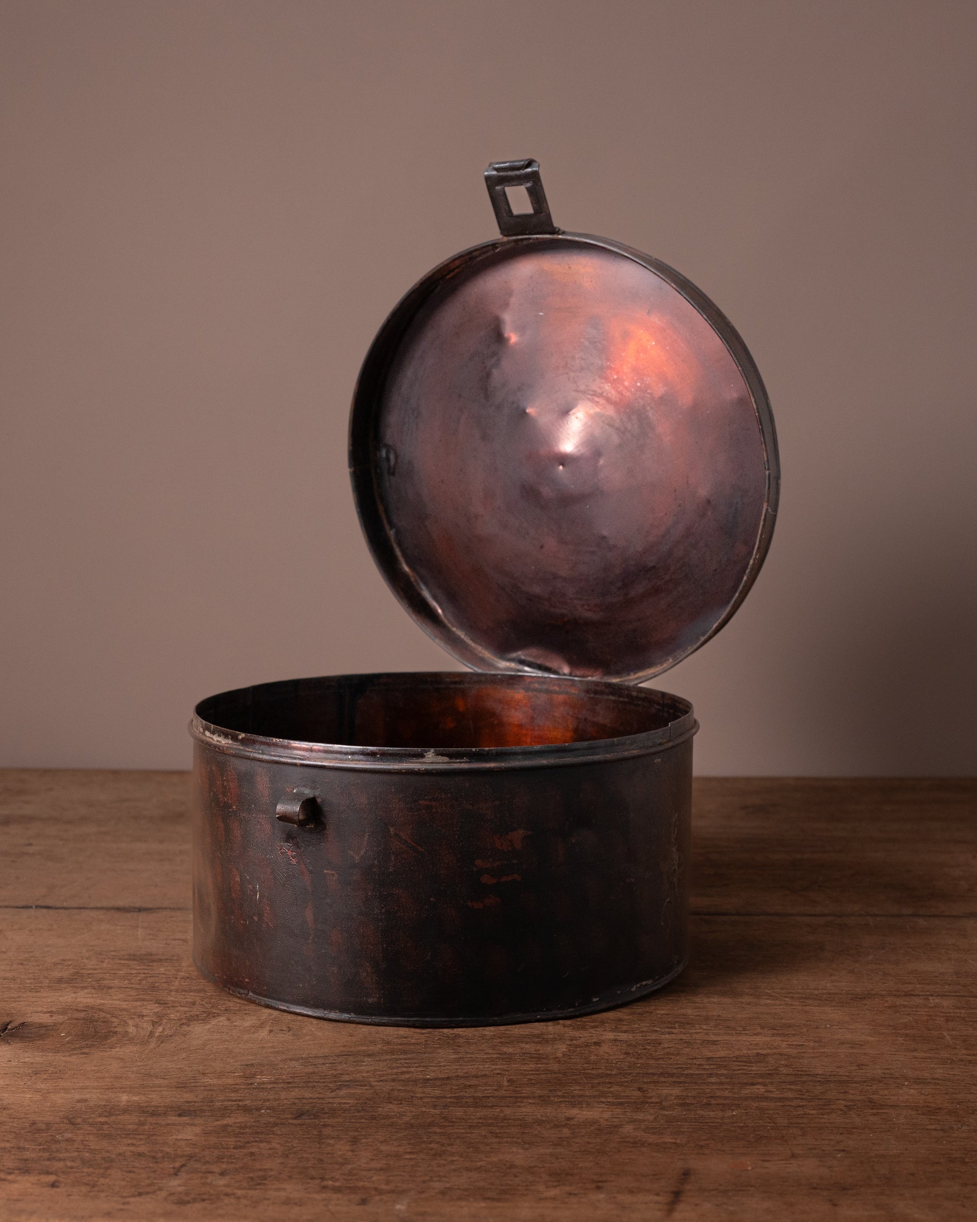 Vintage-style metal hat box with open lid on a wooden surface