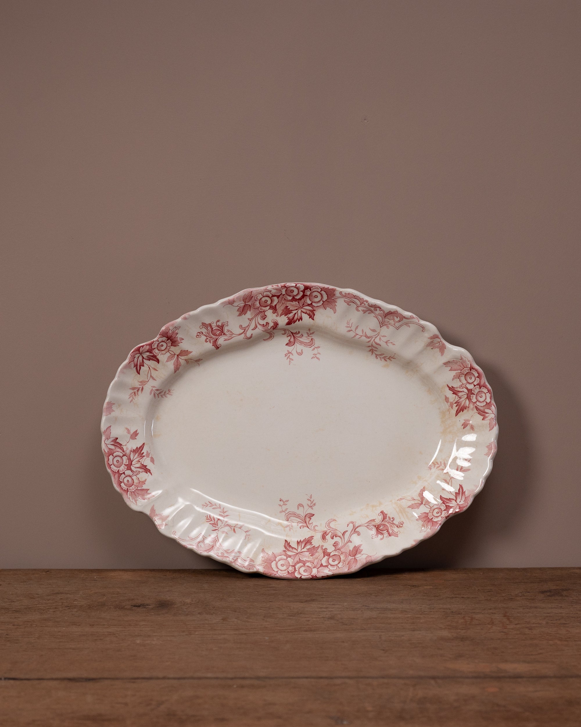 Decorative oval plate with red floral pattern on a wooden surface and brown background