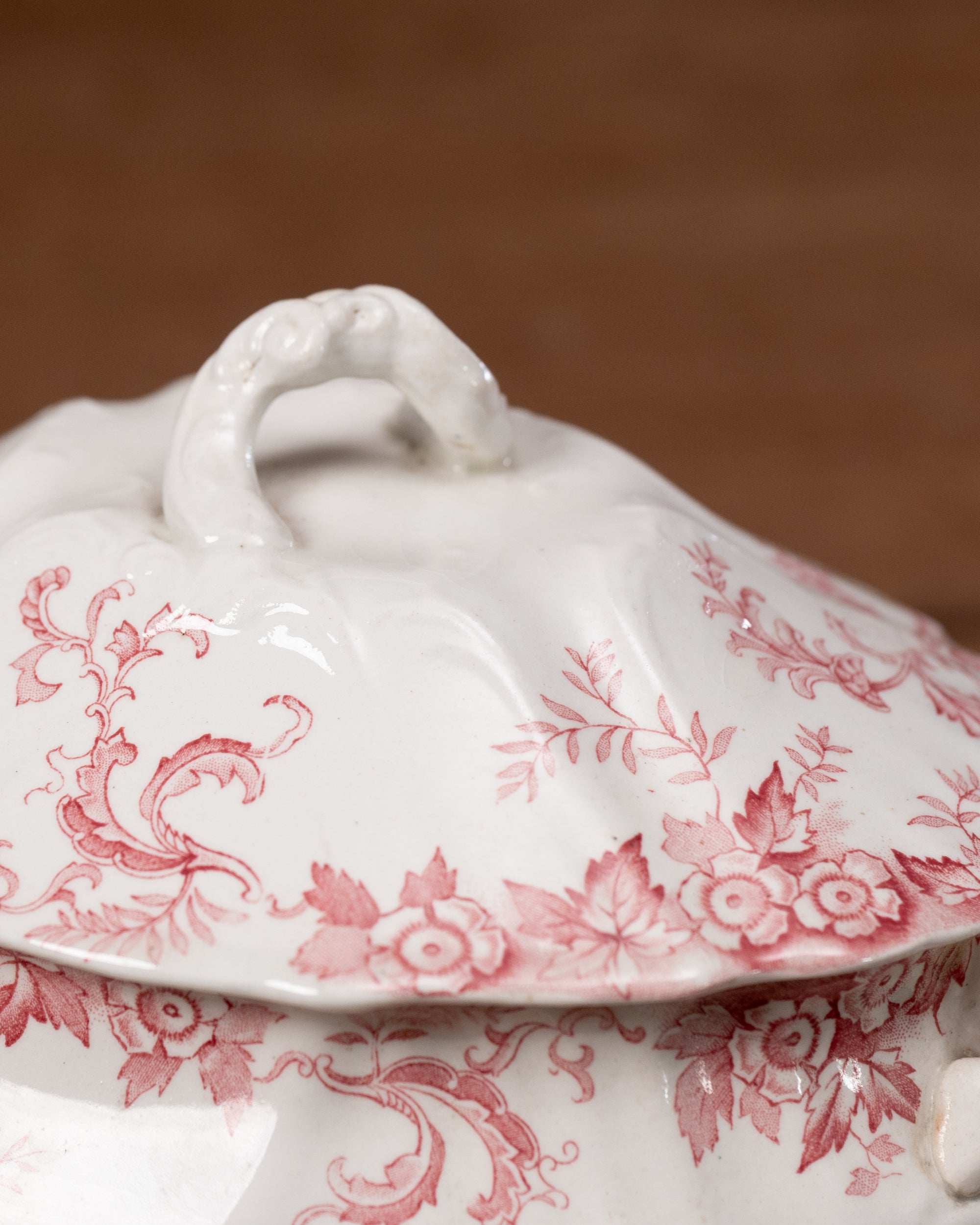 White ceramic tureen with red floral patterns on a brown background