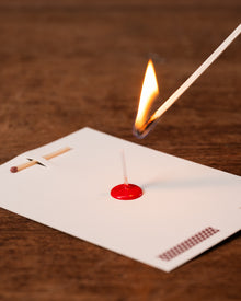 Matchstick being lit with a red matchbox on a wooden surface