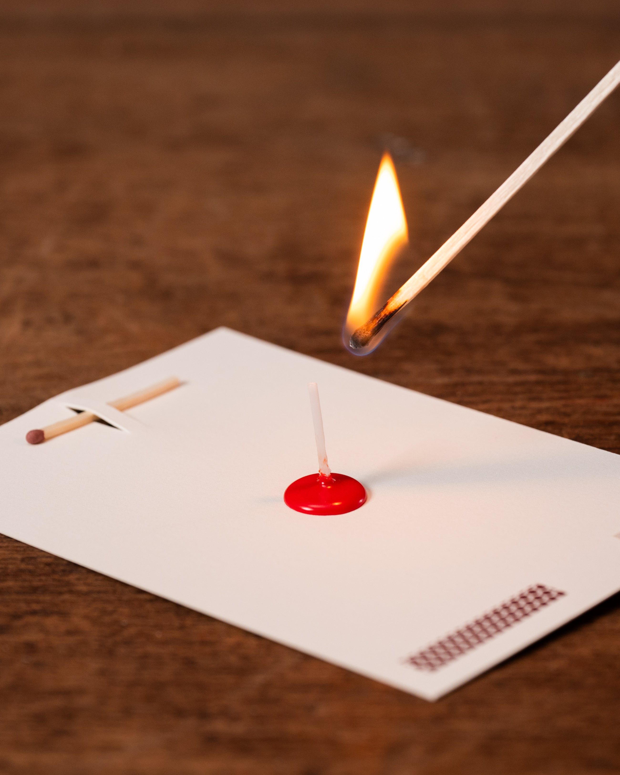 Matchstick being lit with a red matchbox on a wooden surface