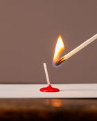 Matchstick being lit with a red matchbox on a white surface against a brown background