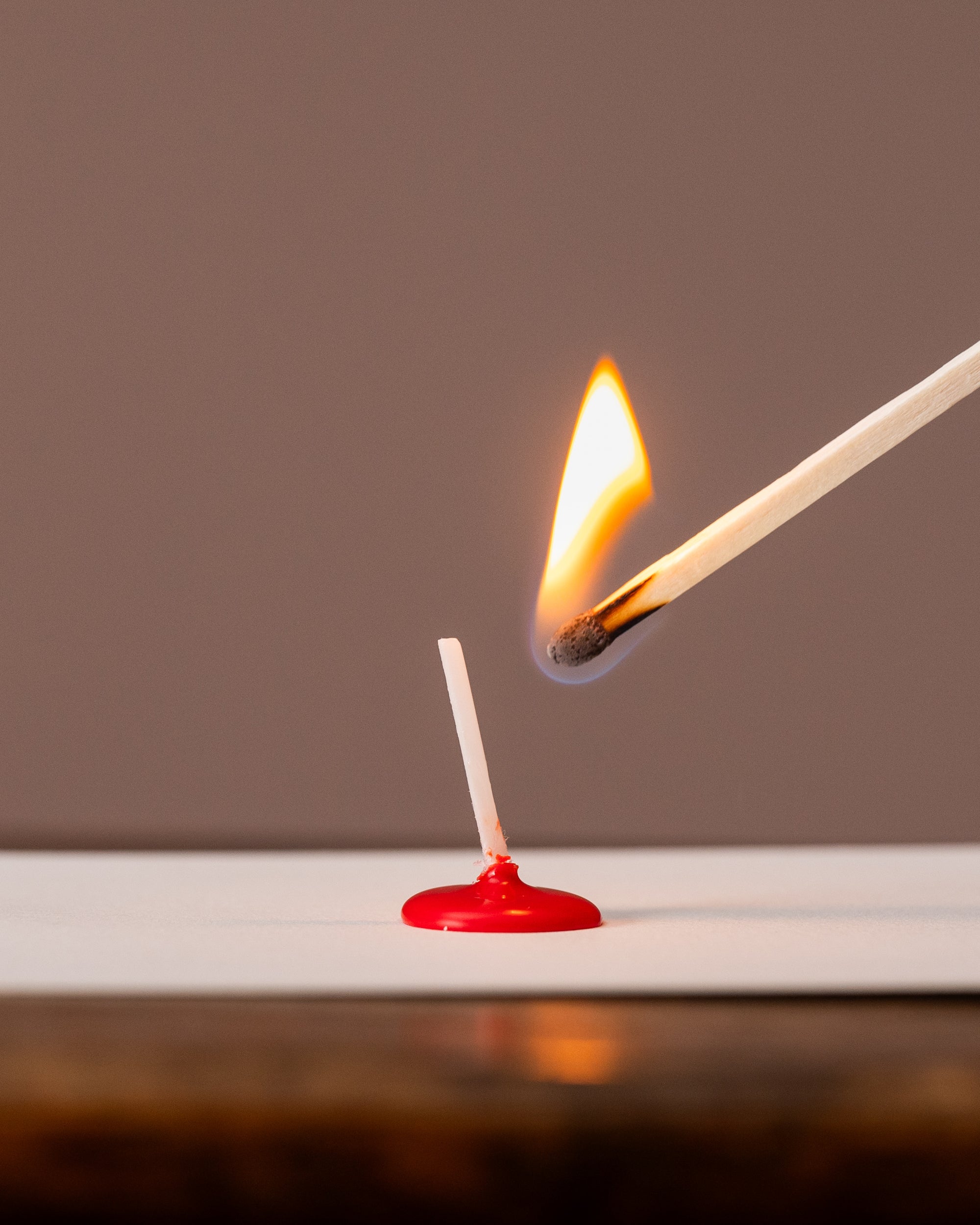 Matchstick being lit with a red matchbox on a white surface against a brown background