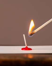 Matchstick being lit with a red matchbox on a white surface against a brown background