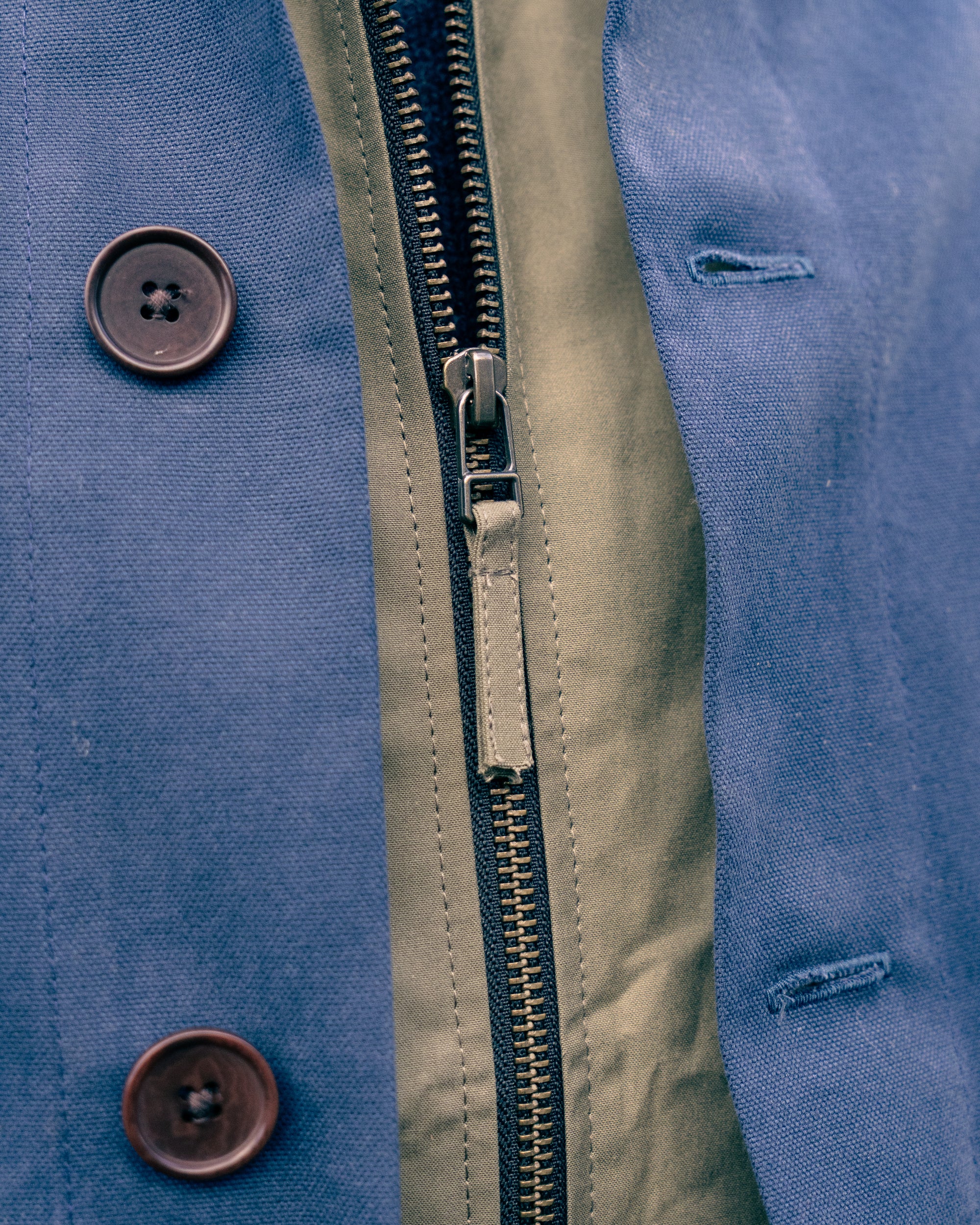 Close-up of a blue jacket with a zip and buttons.