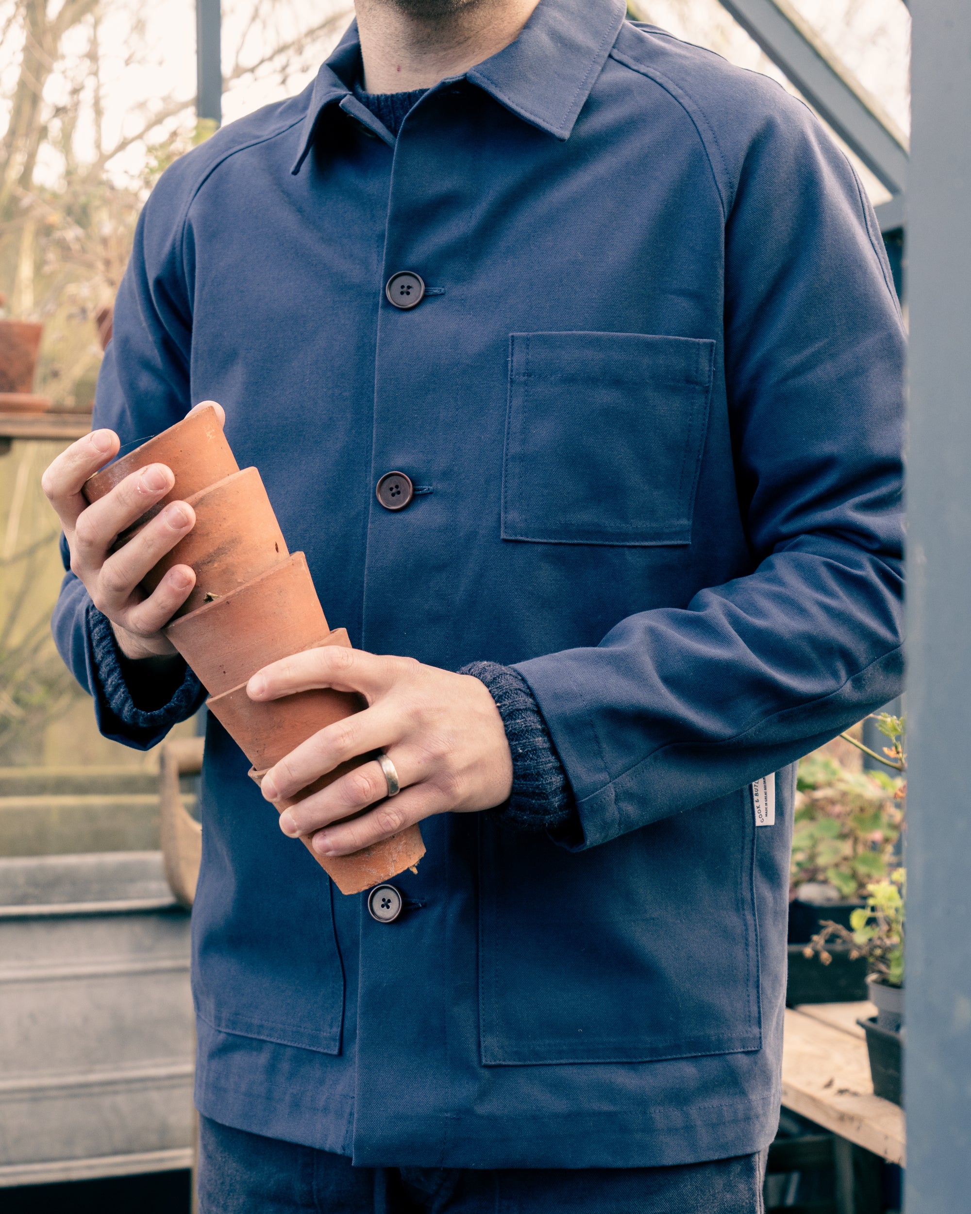 Person wearing a blue Cook & Butler work jacket holding a terracotta pot.